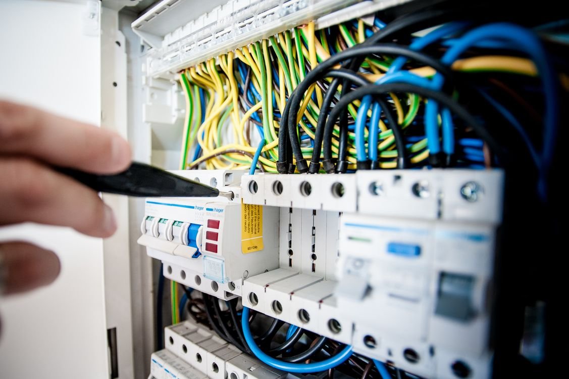 Mão de eletricista trabalhando em quadro de disjuntores com fios coloridos